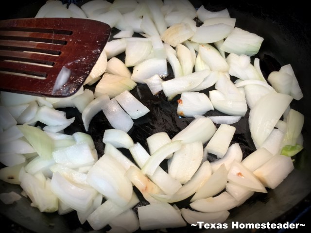 Sauté onions in a black cast-iron skillet using a wooden spatula. #TexasHomesteader