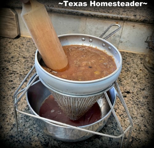 Concord grapes through metal jelly sieve with wooden plunger to separate juice and pulp from skin and seeds for homemade grape jelly. #TexasHomesteader