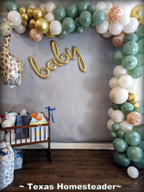 Baby Shower photo op area with seafoam green and gold balloons, giraffe baloon, baby decor and Jenny Lind cradle to hold gifts. #TexasHomesteader